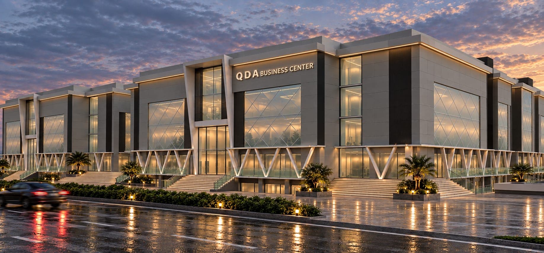 The QDA Business Center at dusk, seen from the street corner, its stone and glass frontage lit from within